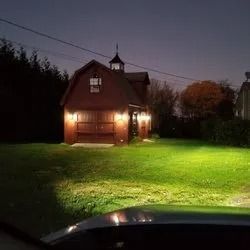 A brown barn with a cupola is lit by lights at night, in a grassy field.