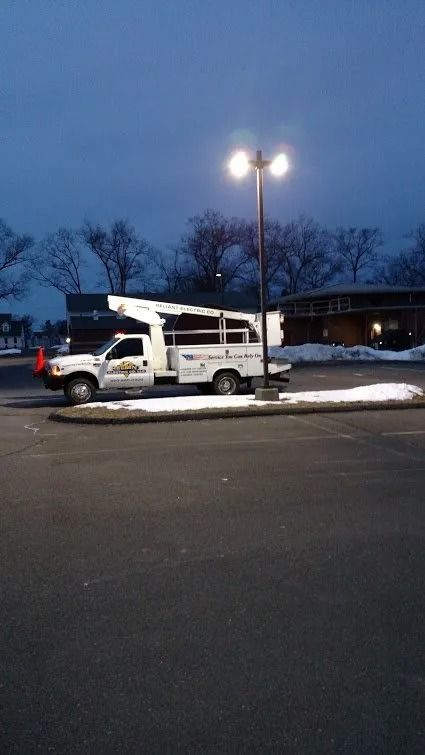 White utility truck with boom lift parked near a streetlight, snowy ground, and a building at dusk.