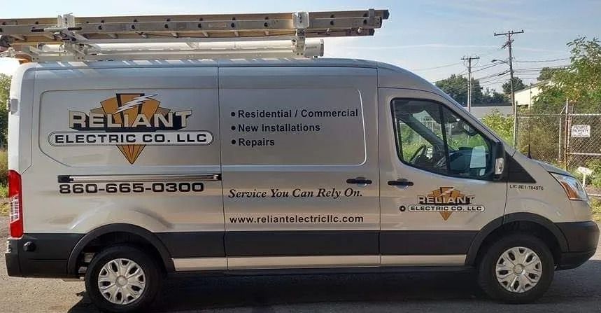 Silver and black Reliant Electric Co. van parked, ladder on top, text details on side.