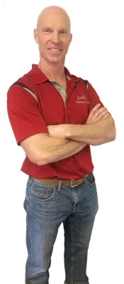A man wearing a red polo shirt and blue jeans with arms crossed smiling.