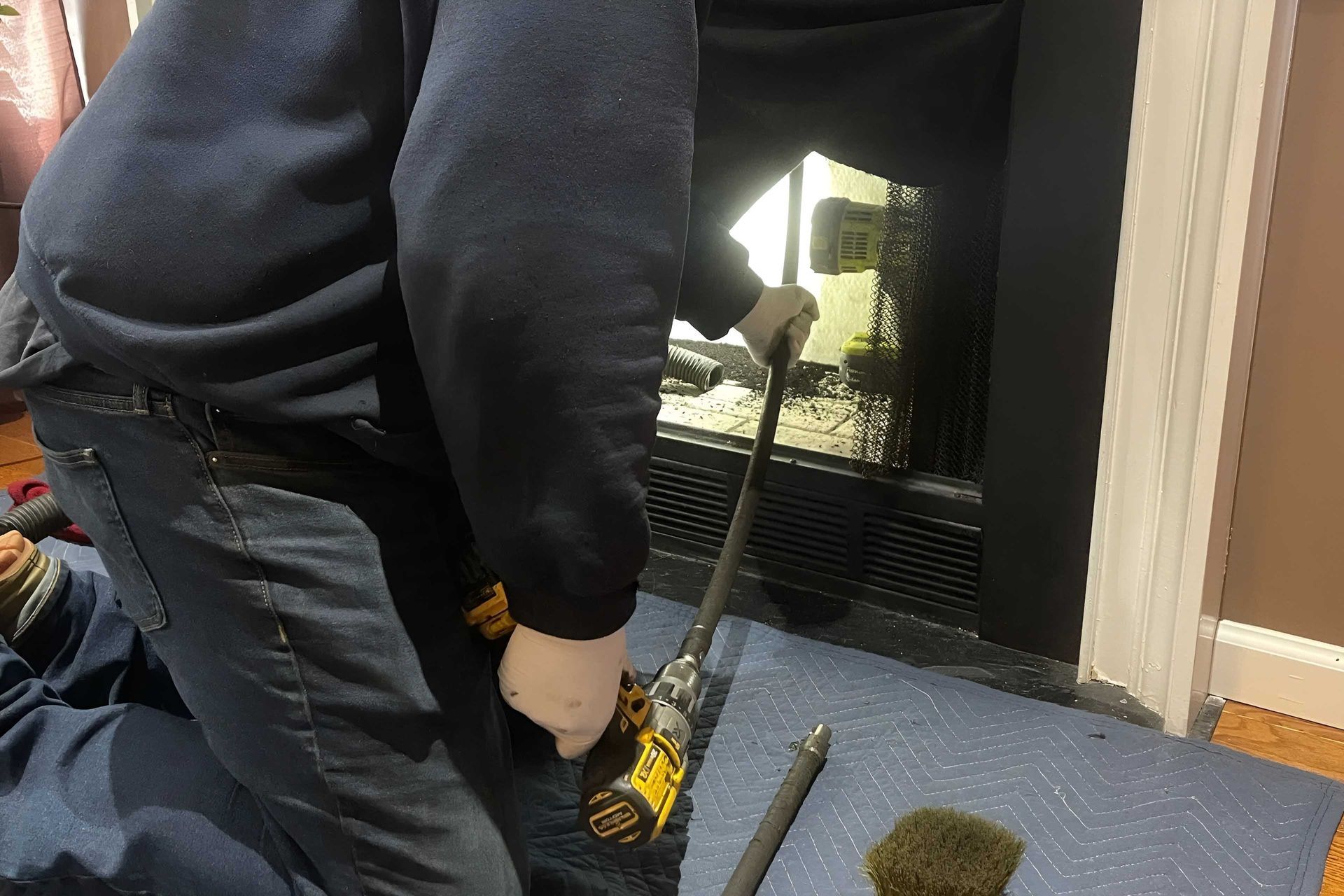 Person cleaning a fireplace with a tool and a vacuum, in a home setting.