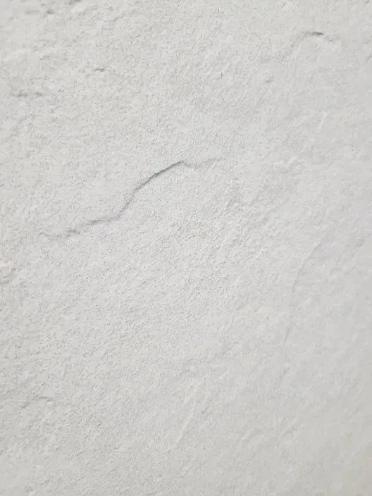 Close-up of a light gray textured wall with a faint crack running diagonally.