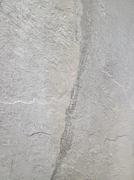 Close-up of a light gray textured stone wall with a vertical crack