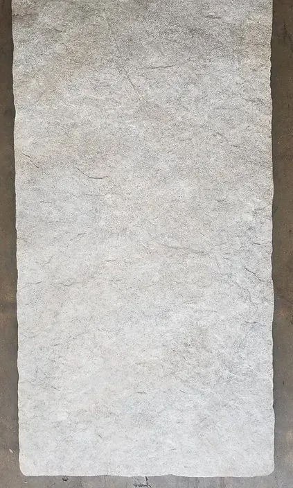 Vertical light gray textured stone slab with rough edges on a neutral background