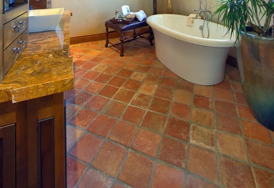 Bathroom with terracotta tile floor, clawfoot tub, stone sink, and wooden vanity.