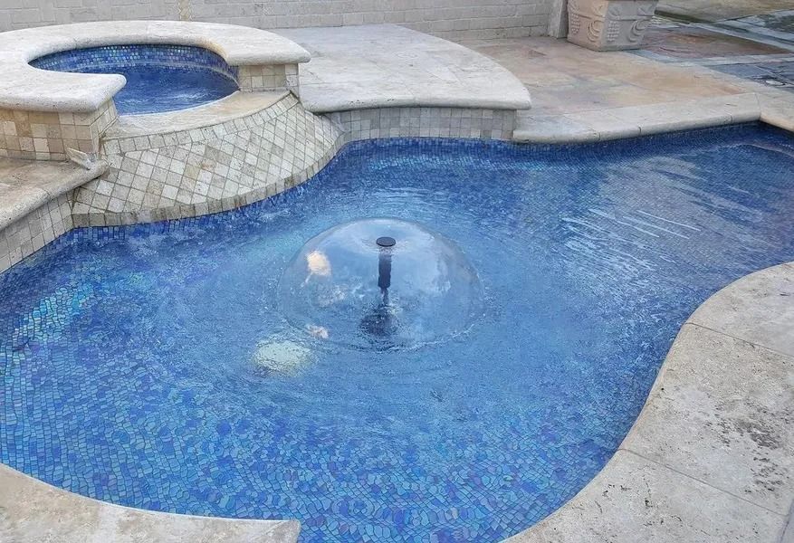 Blue backyard pool with a small raised spa and stone deck surrounding it