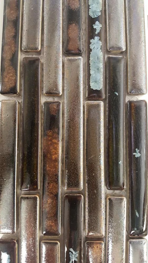 Close-up of bronze and brown metal tiles in a vertical mosaic pattern with blue-green patina spots