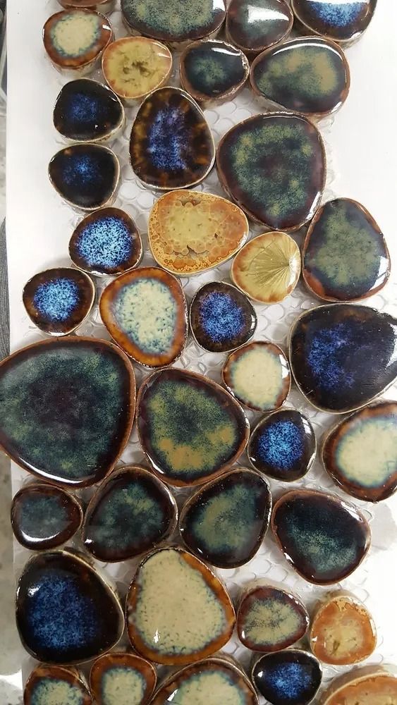 Multicolored pebbles with glossy blue, green, gold, and brown surfaces in a clustered pattern