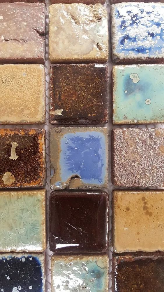 Close-up of assorted glossy mosaic tiles in muted blue, brown, cream, and green tones.