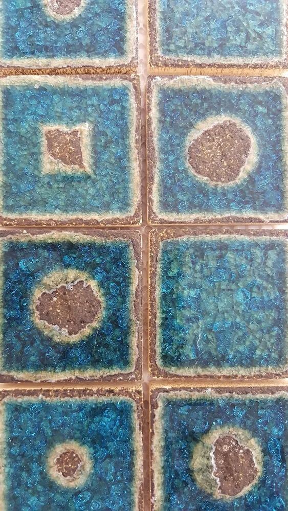 Blue tiled wall with tan grout and inset squares and circles in muted brown and white