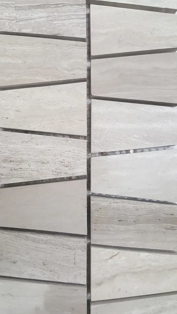 Close-up of light gray stone wall with horizontal stacked tiles and dark grout lines.