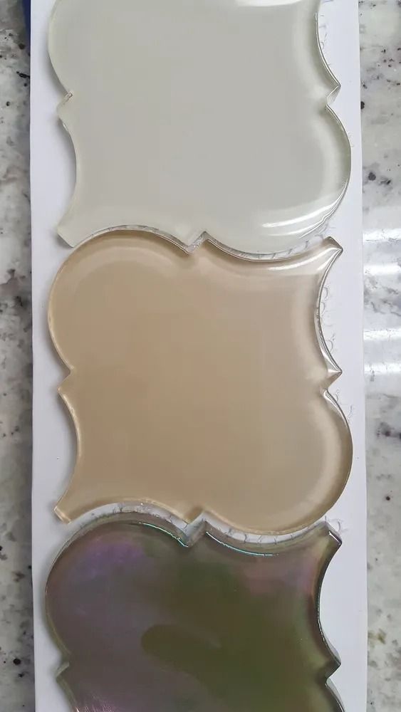 Three scalloped cosmetic pans stacked vertically: white, beige, and iridescent green-purple.