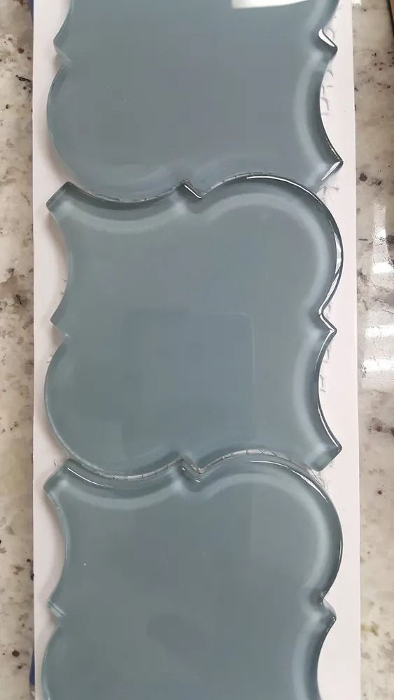 Three stacked gray decorative wall tiles with scalloped edges on a white surface