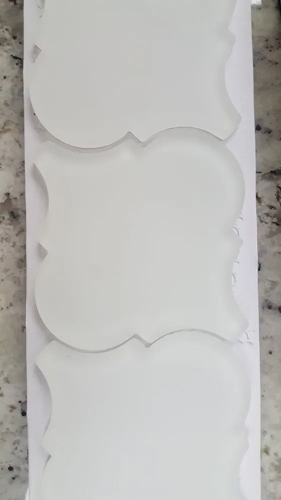 Three stacked white decorative wall panels with scalloped edges on a light surface