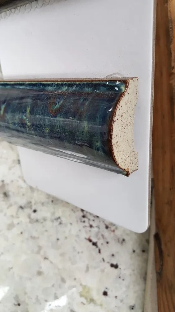 Close-up of a blue-gray metal pipe edge against a white board and wooden wall trim.