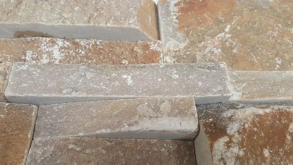 Close-up of tan and beige stone pavers with a long gray plank laid across them