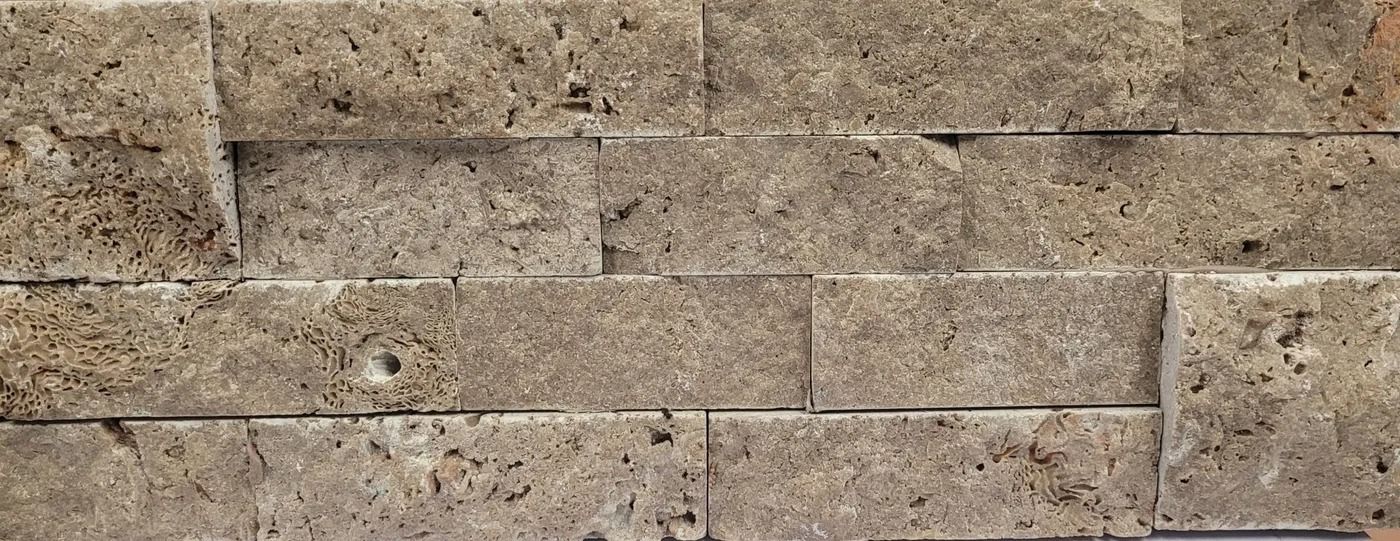 Close-up of a tan stone brick wall with rough texture and horizontal mortar lines
