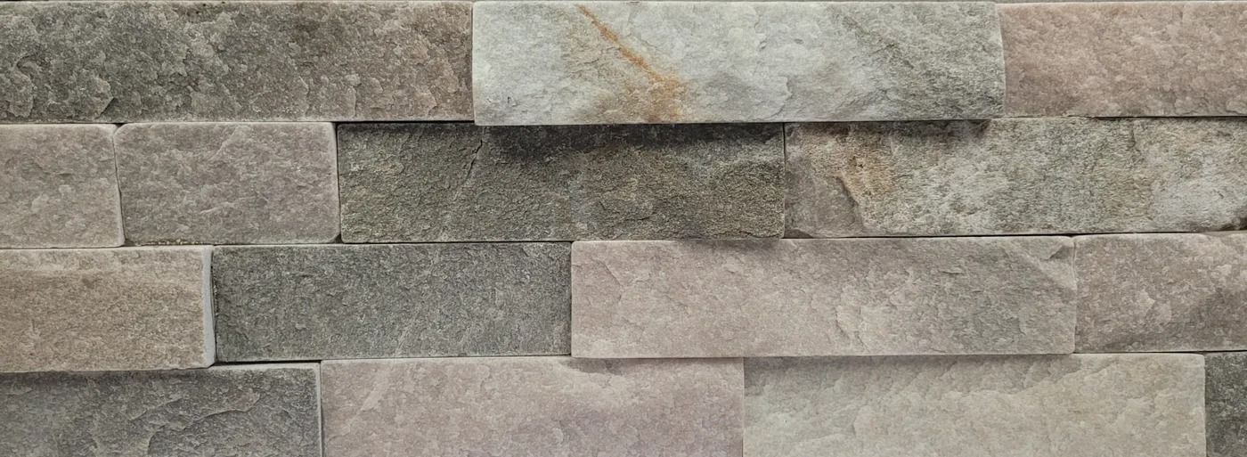 Close-up of a stacked stone wall with gray, beige, and tan rectangular stones.