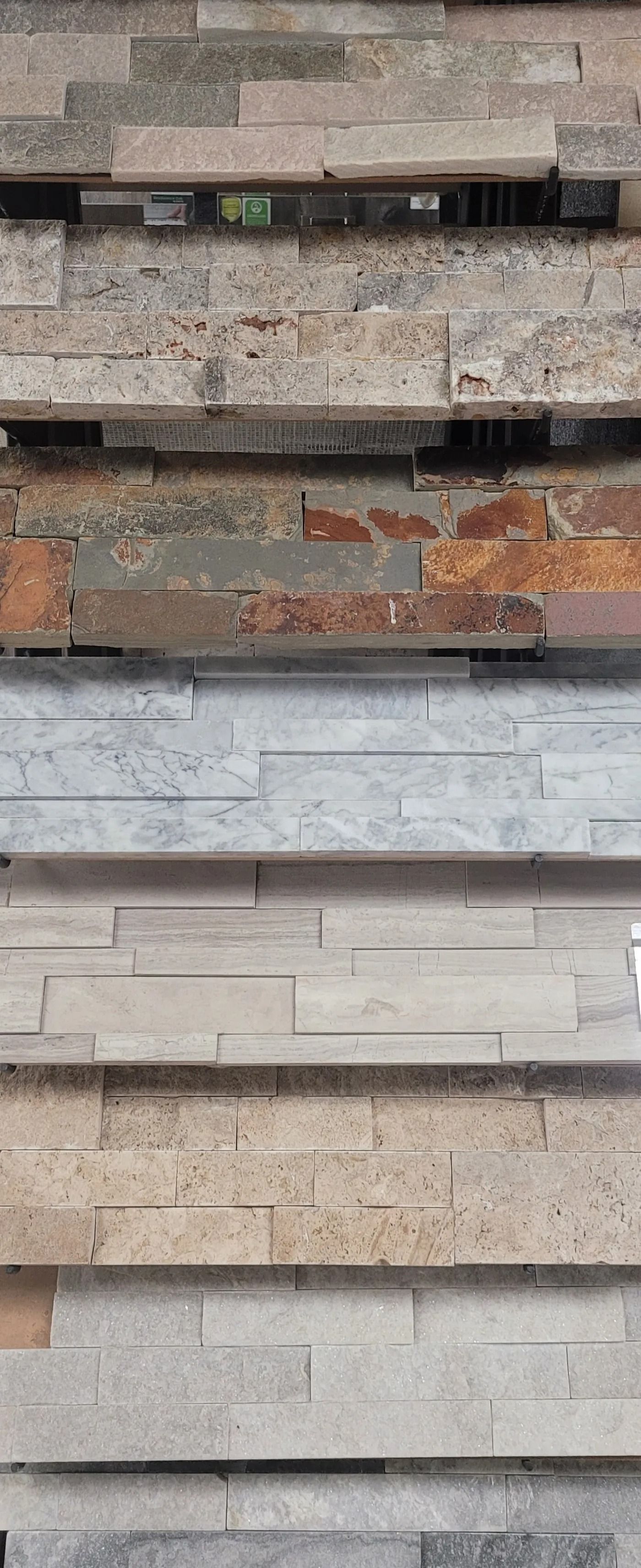 Stacked samples of textured stone and tile wall panels in gray, beige, and rust tones.