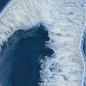 Aerial view of dark blue water bordered by white ice along a curved shoreline
