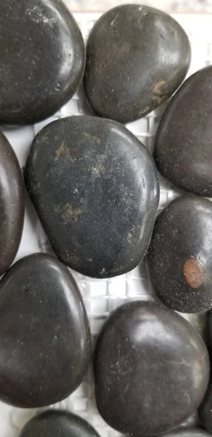 Close-up of smooth dark gray pebbles, with one small orange-brown stone visible