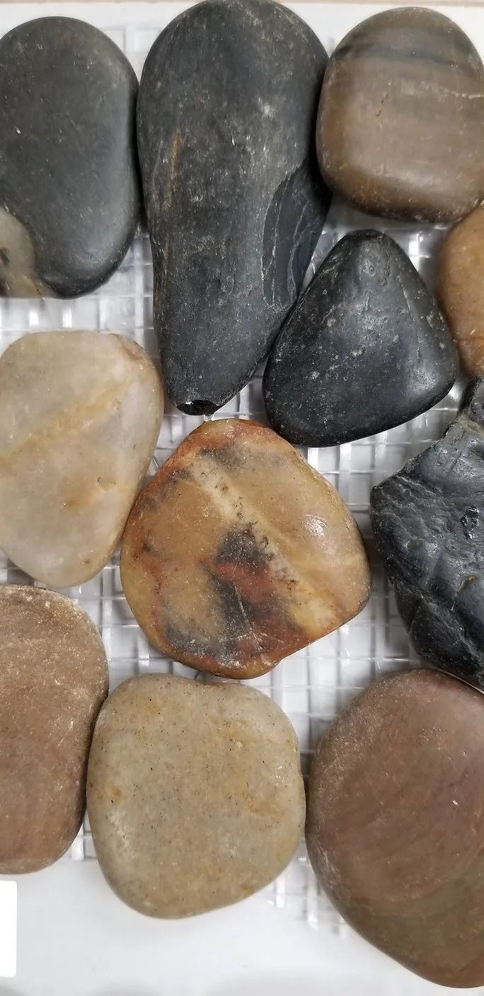 Assorted smooth pebbles in black, tan, brown, and gray on a light striped surface.
