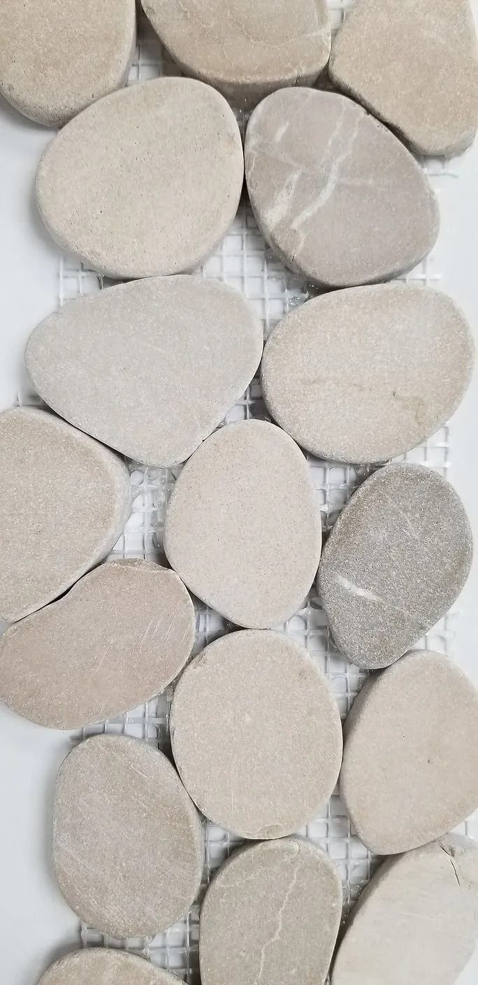 Close-up of smooth oval pebbles in beige and gray tones, arranged in a tight pattern.