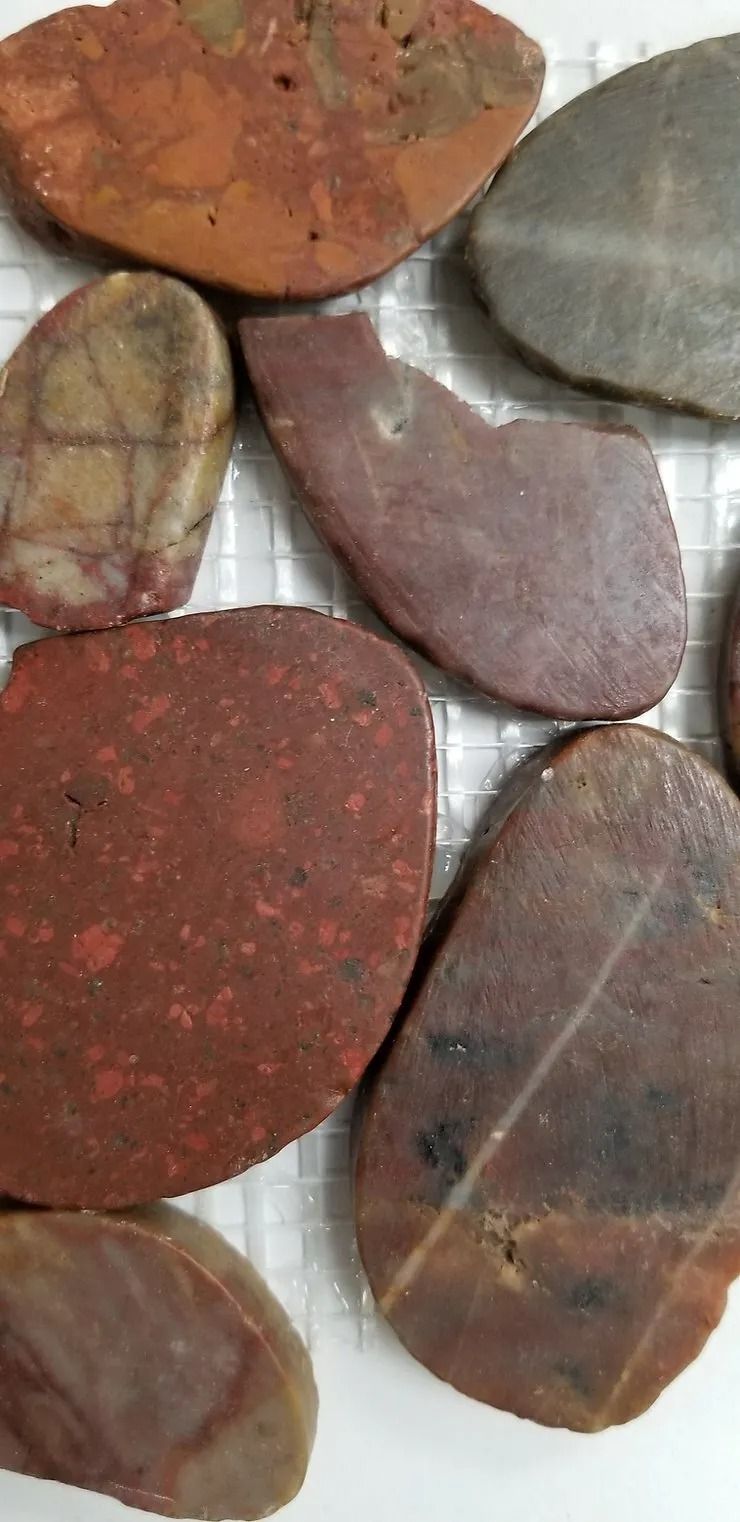 Assorted smooth pebbles in red, brown, and gray tones, tightly arranged against a light background