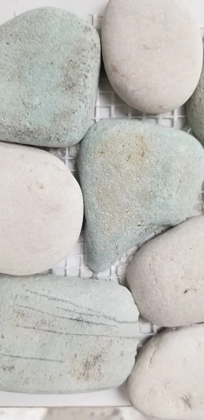 Close-up of smooth light gray and pale green pebbles stacked in a wall pattern