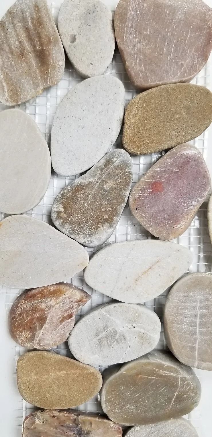 Close-up of smooth oval pebbles in beige, white, and tan tones arranged in a mosaic pattern.