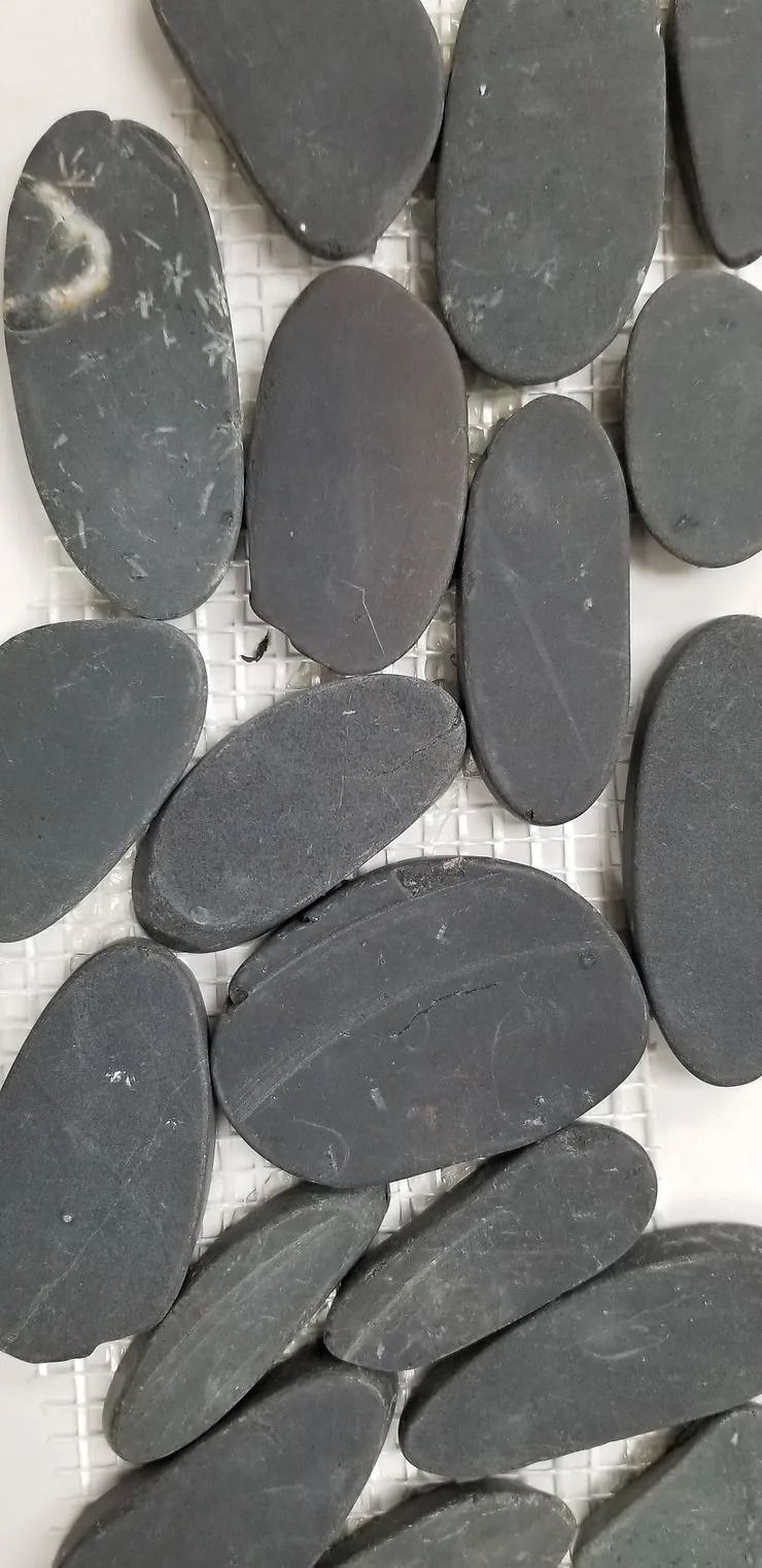 Flat gray pebbles arranged in a close-up pattern, with a few lighter stones among them