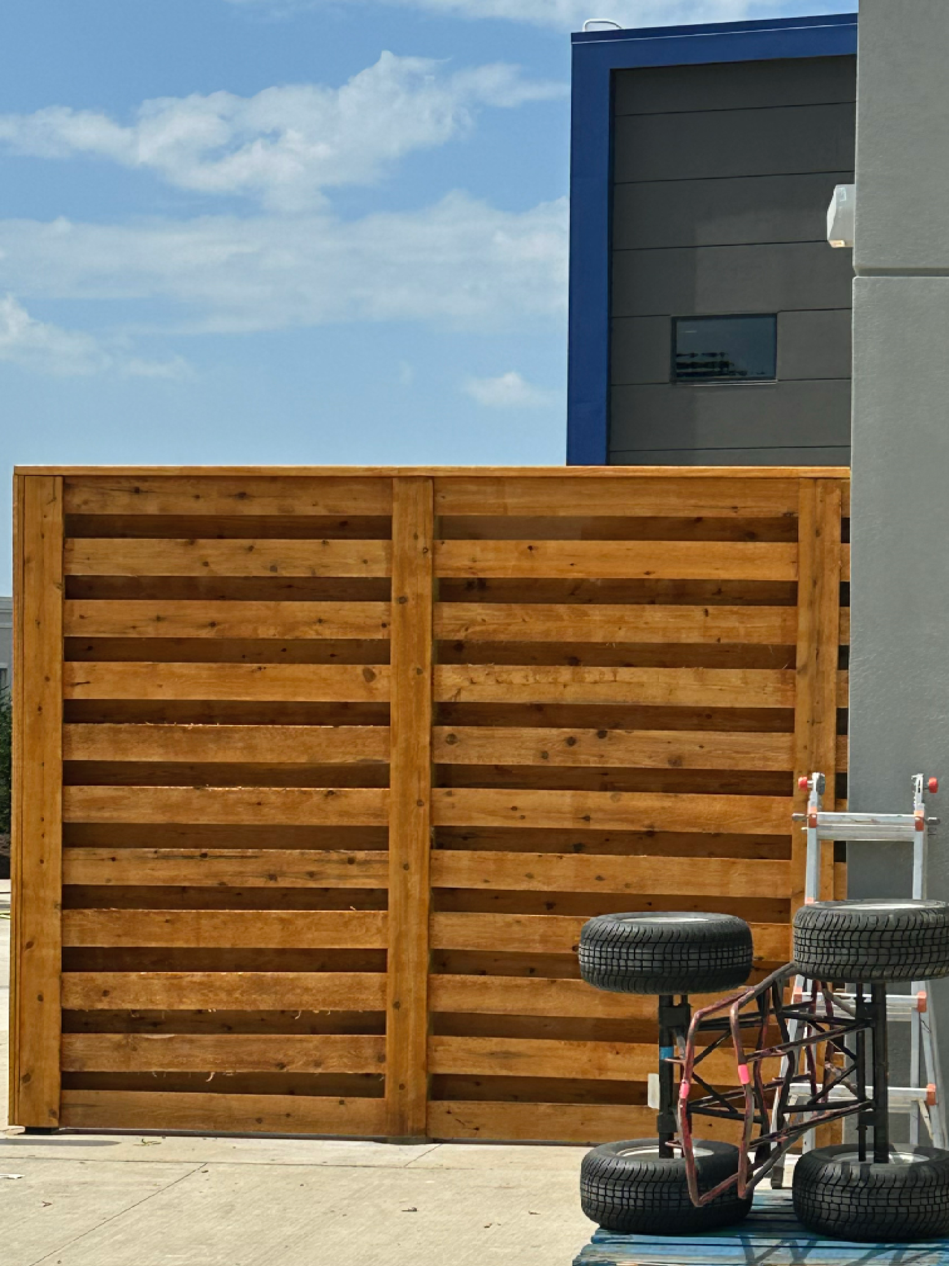 Wooden fence, blue building background, car tires on the ground.