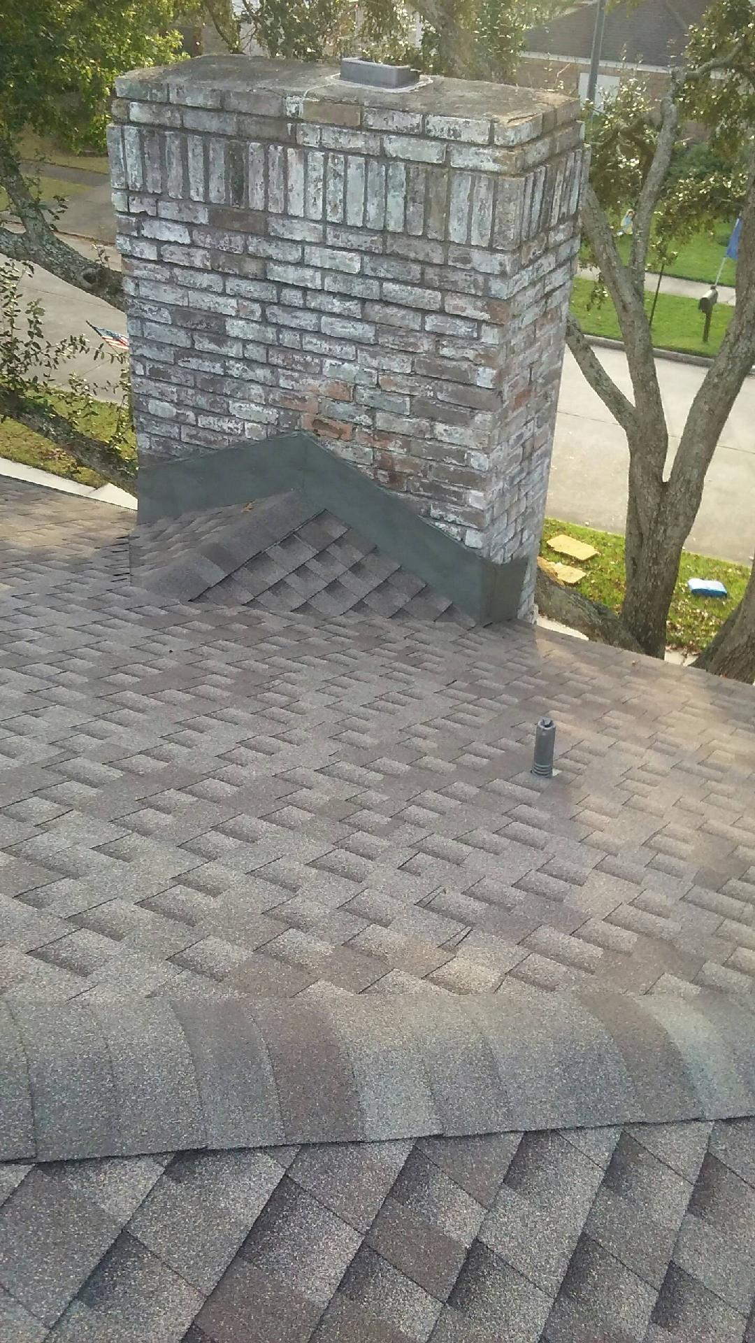 A brick chimney on top of a roof next to a tree.