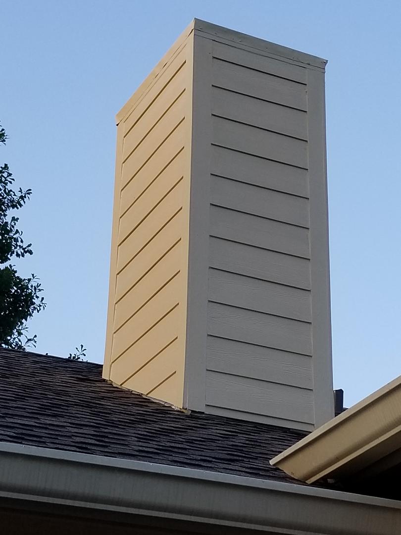 A chimney on the roof of a house with a tree in the background