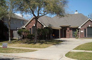 A brick house with a gray roof and a tree in front of it.