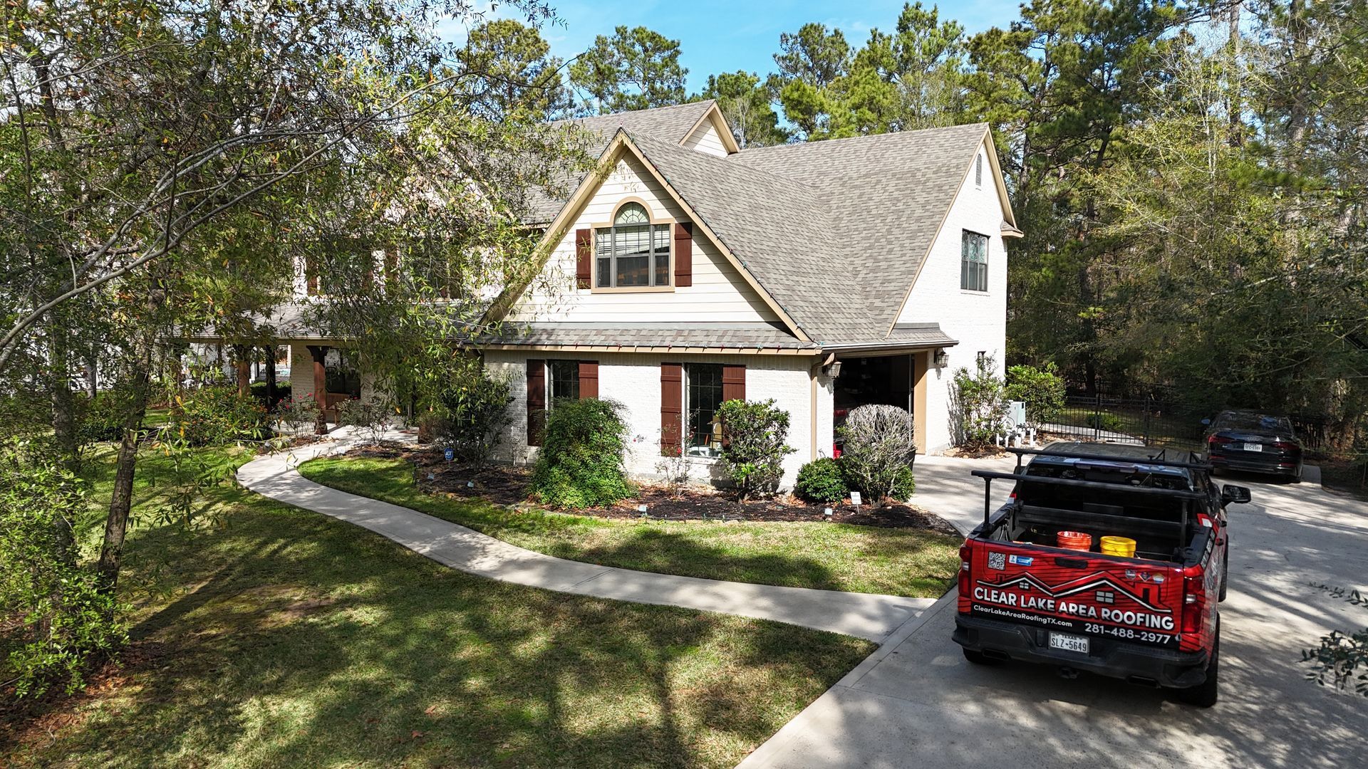 A white house with a brown roof and red truck parked in front.