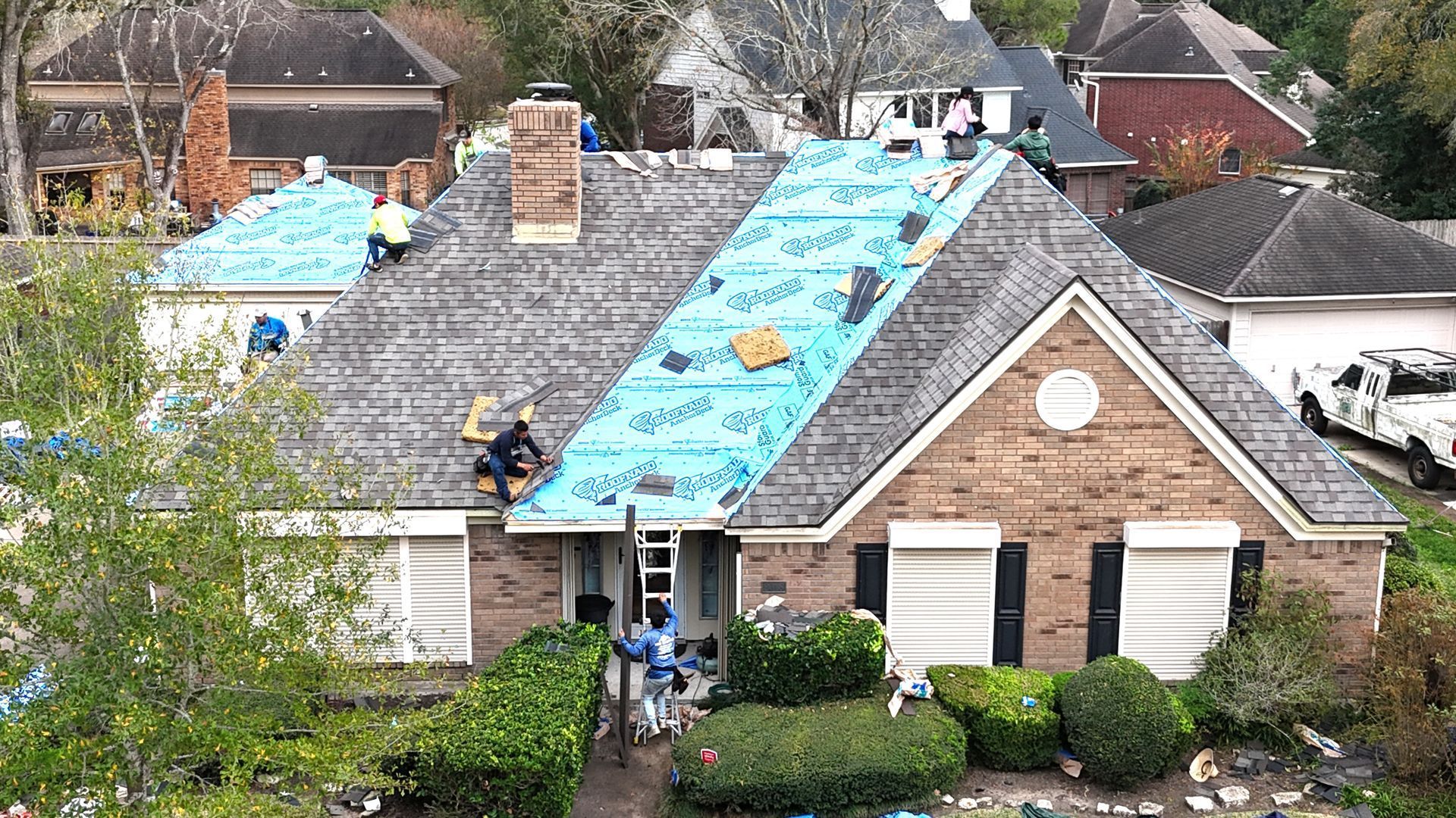 Roofers working on a house, covering it with blue underlayment and shingles.