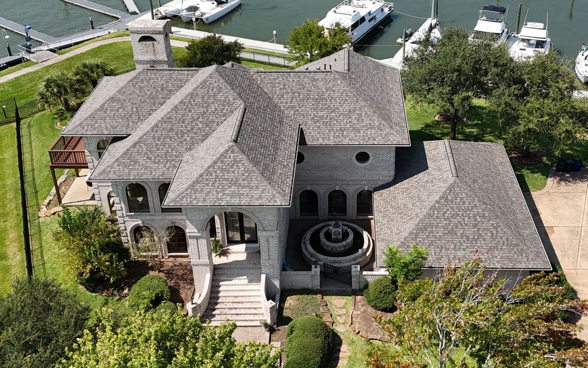 Aerial view of a large stone house with a complex roof near a marina with boats.