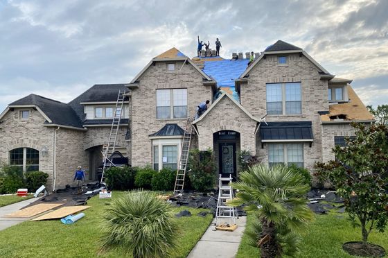 A large brick house is being remodeled with a blue tarp on the roof.