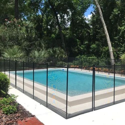 Backyard swimming pool enclosed by a black safety fence, surrounded by trees and greenery