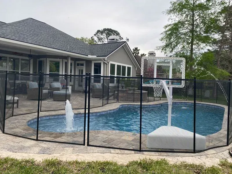 Backyard swimming pool with safety fence, stone patio, and house patio in the background