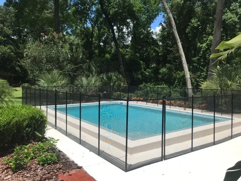 Outdoor swimming pool surrounded by a black safety fence and trees
