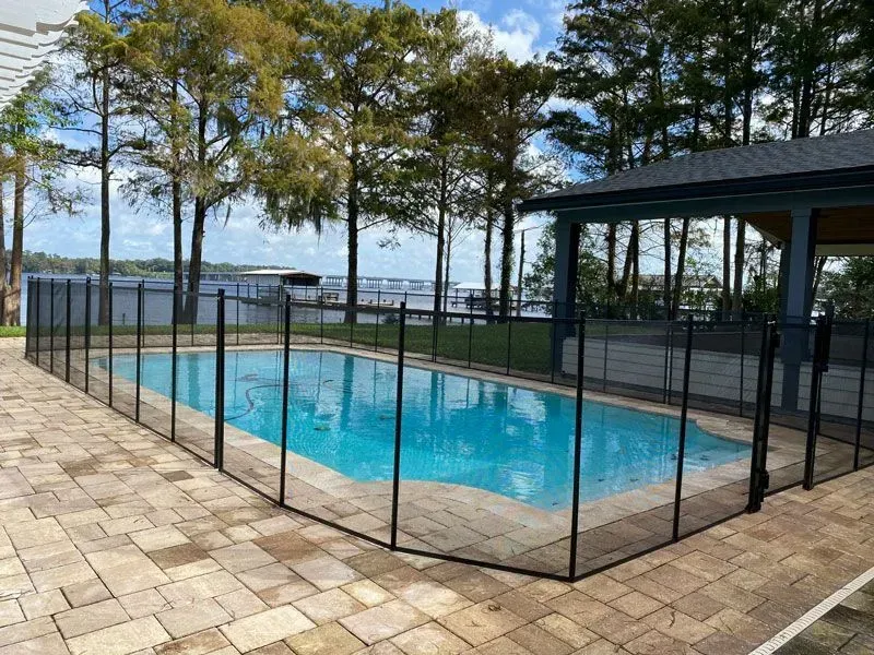 Outdoor pool surrounded by black safety fencing, with trees and a lake view beyond.