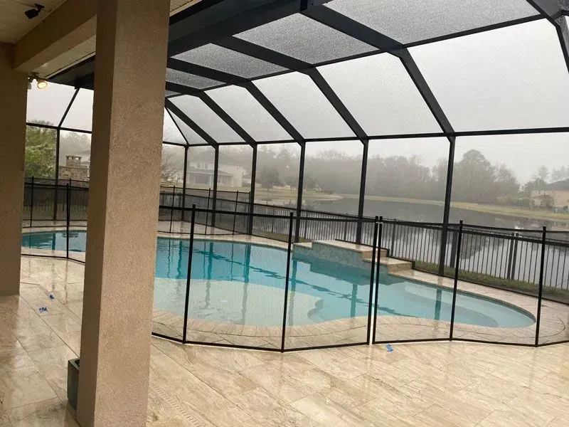 Screened-in pool area with covered patio and rainy, overcast view beyond the fence