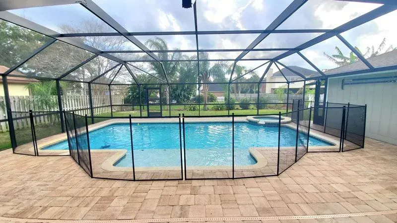 Screened-in backyard swimming pool with blue water, brick patio, and palm trees beyond the fence