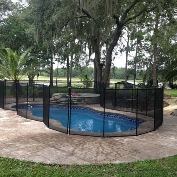 Backyard pool enclosed by a black safety fence, surrounded by stone patio and trees