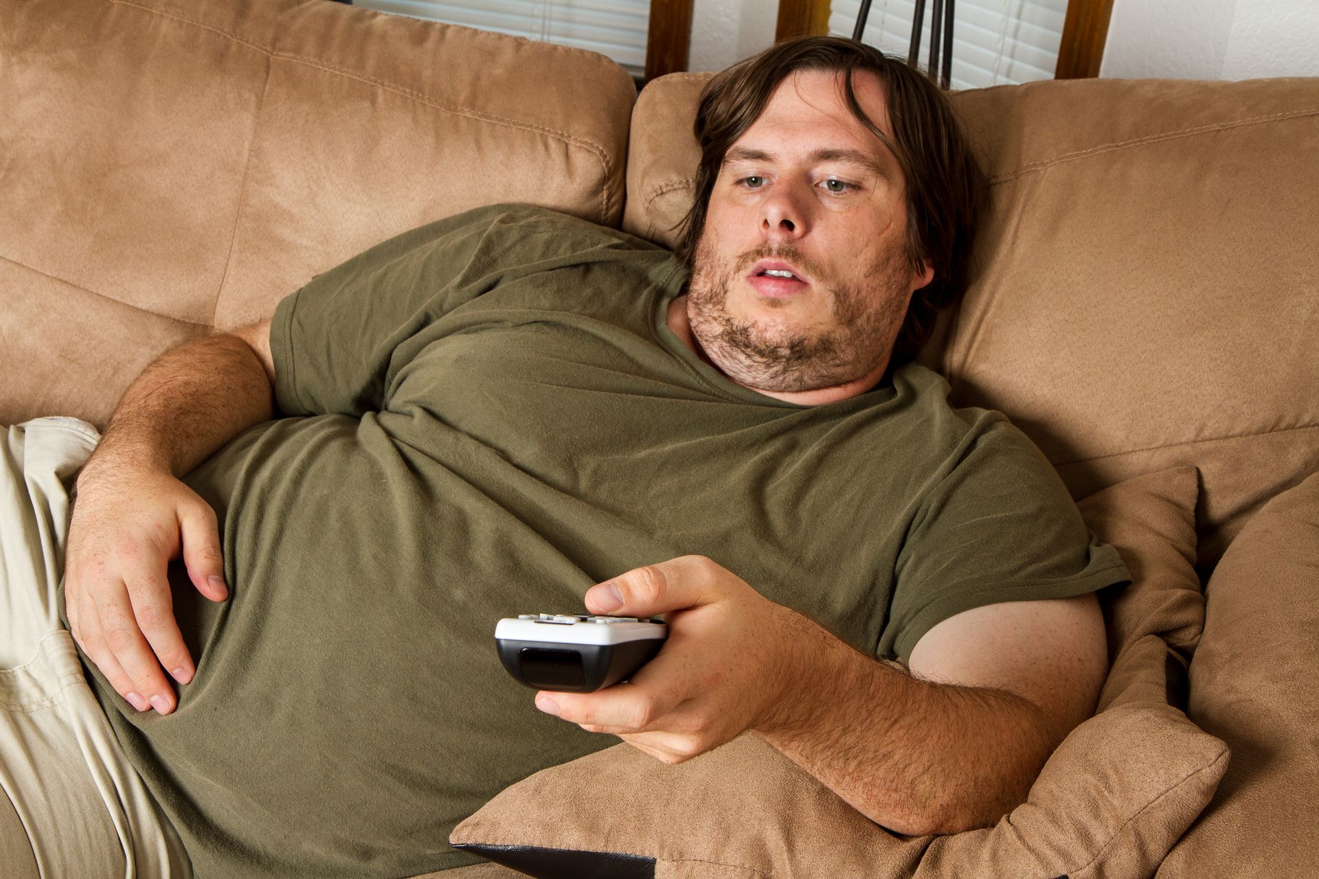 An overweight lazy man on a couch with a remote in his hands.