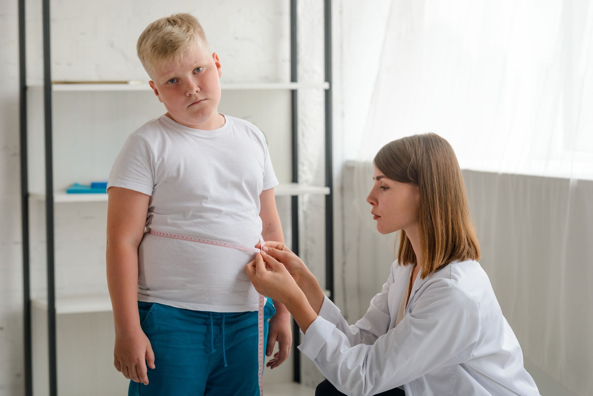 A overweight elementary school kid having his stomach measured with a pink tape measure