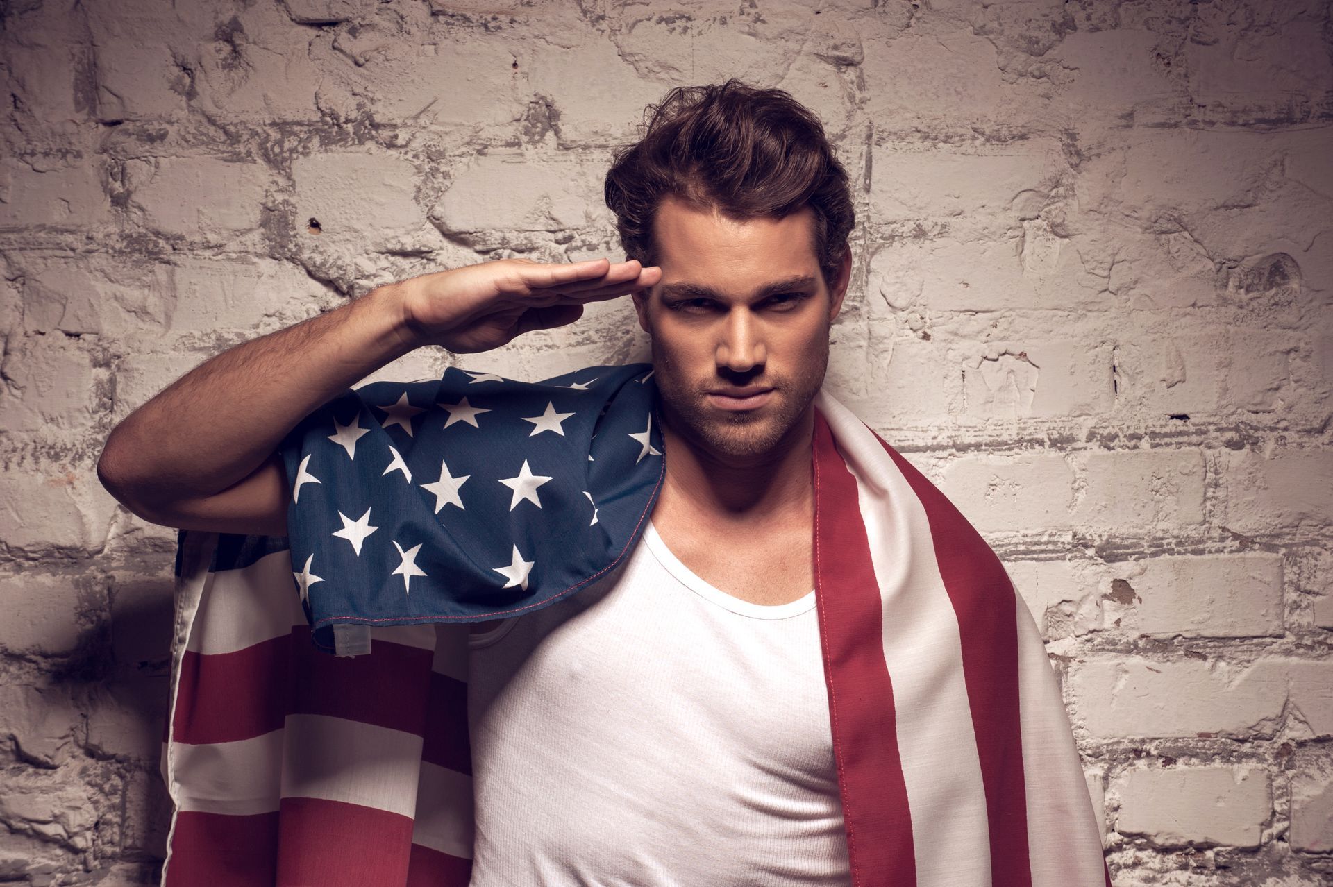 A white man wearing a white tank top with an American flag around his shoulders and back