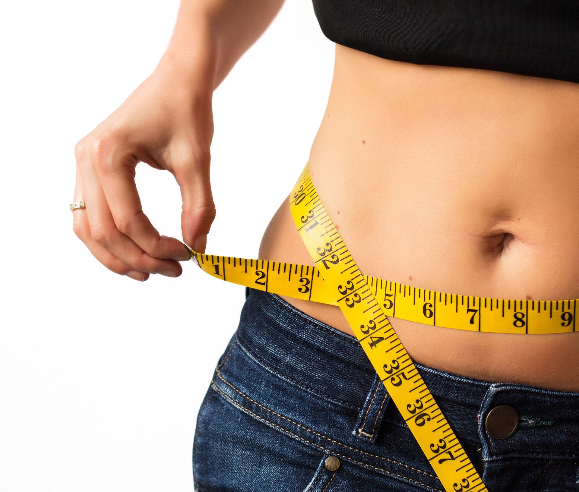 A fit white woman measuring her waist with a yellow tape measure